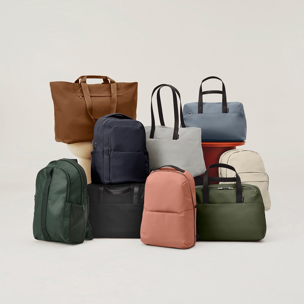 A group of Away backpacks, totes, and duffles in various colors on a white background